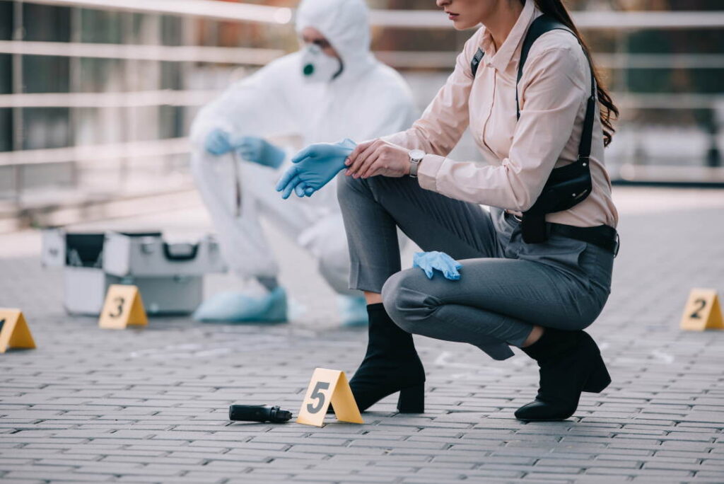 A forensics detective in full protective bodysuit in the background. Casually dressed police detective in the front. What does a detective wear?