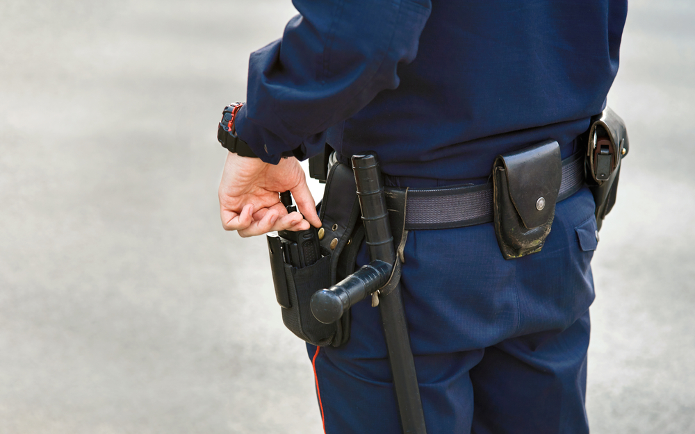 Hand of police officer holding radio set, baton tonfa close up on the belt.