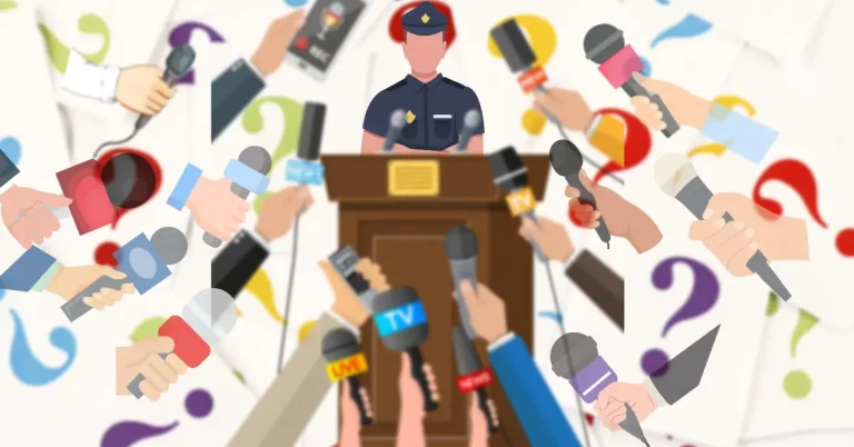 Police officer at a podium surrounded by reporters holding microphones
