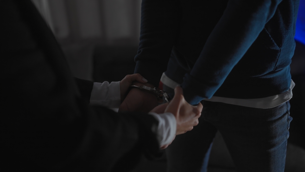 Policewoman handcuffs man indoors depicting an arrest scenario.