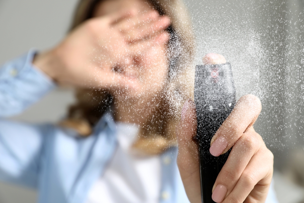 Young woman covering eyes with hand and using pepper spray