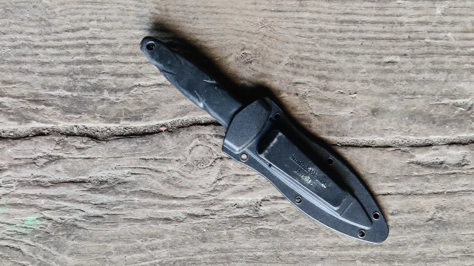 Black fixed-blade duty knife in its sheath on a wooden surface
